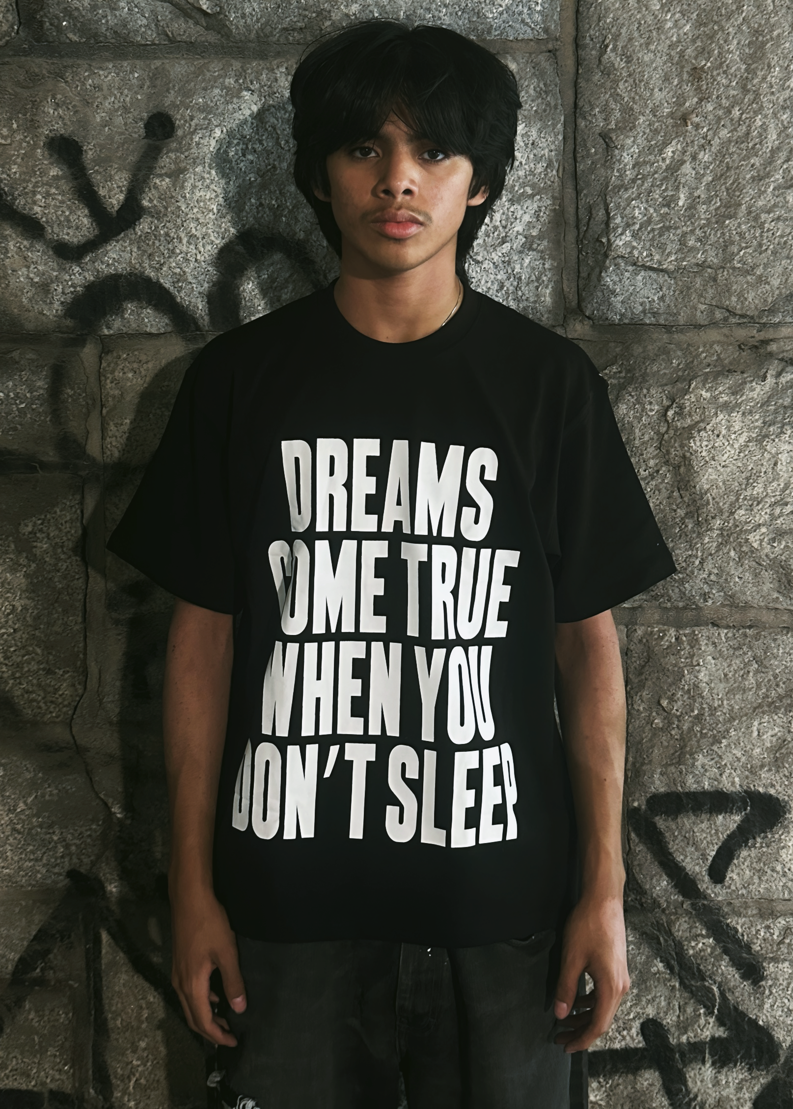 Person wearing a black t-shirt with white text against a textured wall.