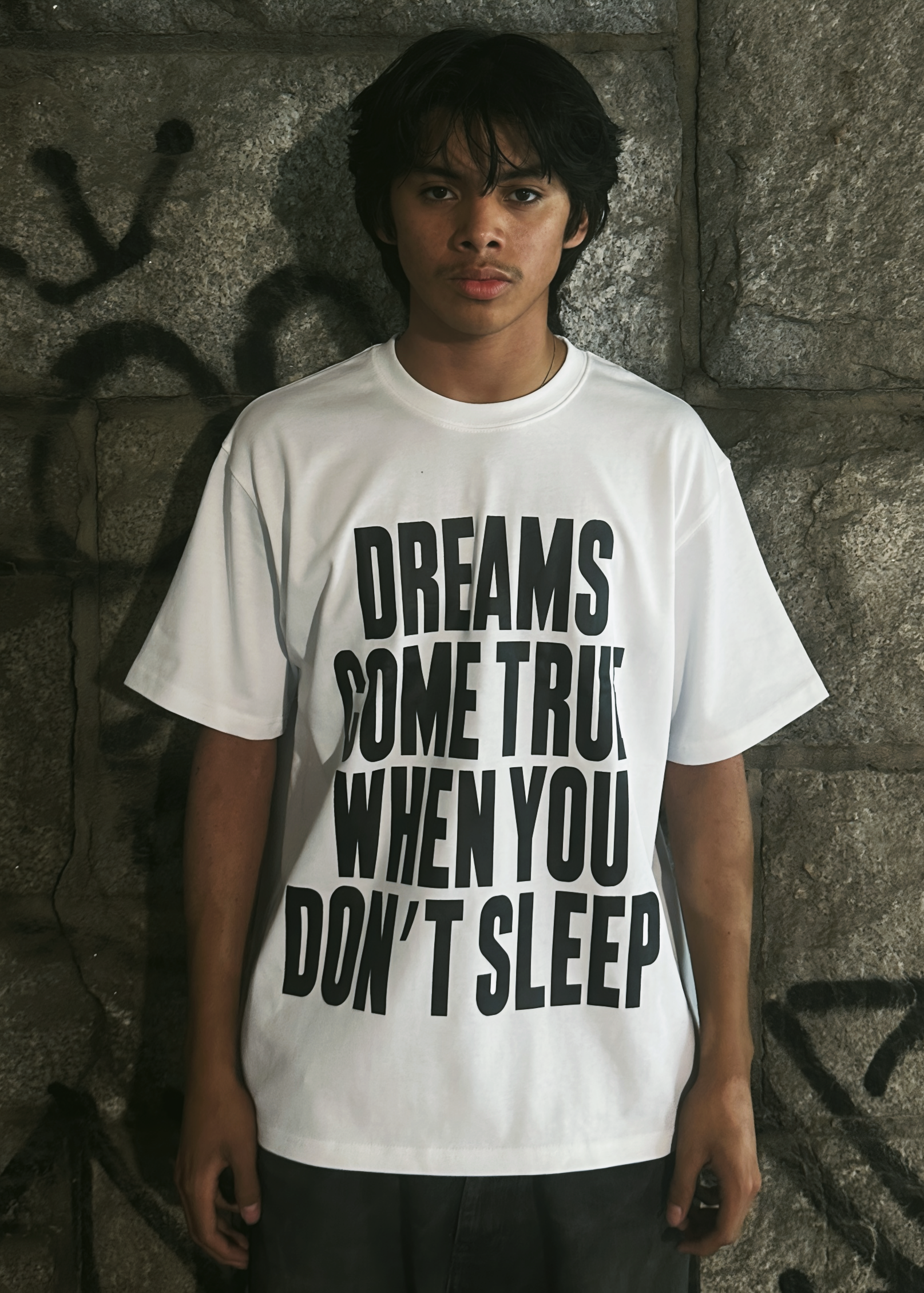 Person wearing a white t-shirt with text against a textured wall.