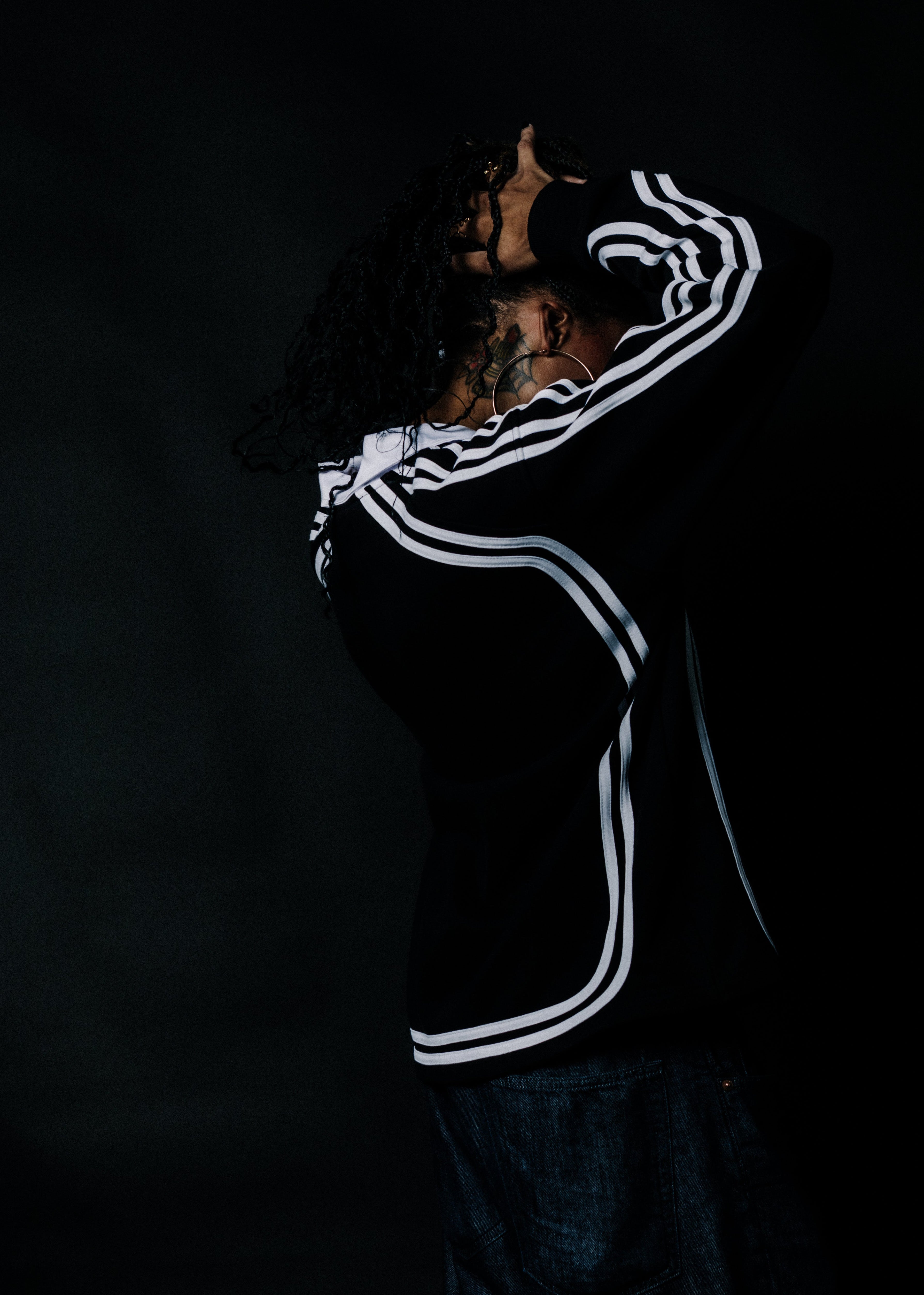 A person in a black hoodie with white stripes on the sleeves and hem, shown from the back against a dark background.